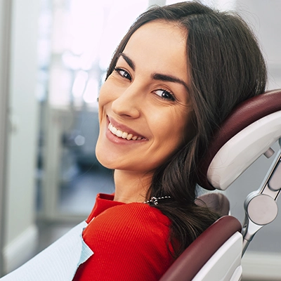uma mulher jovem sorrindo sentada na cadeira odontológica